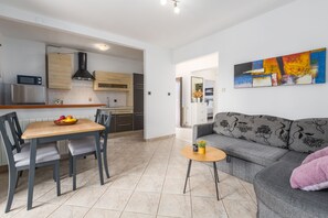 A modern kitchen with built-in appliances, a dining area with a table and chairs, and a living area with a sofa and a painting on the wall.