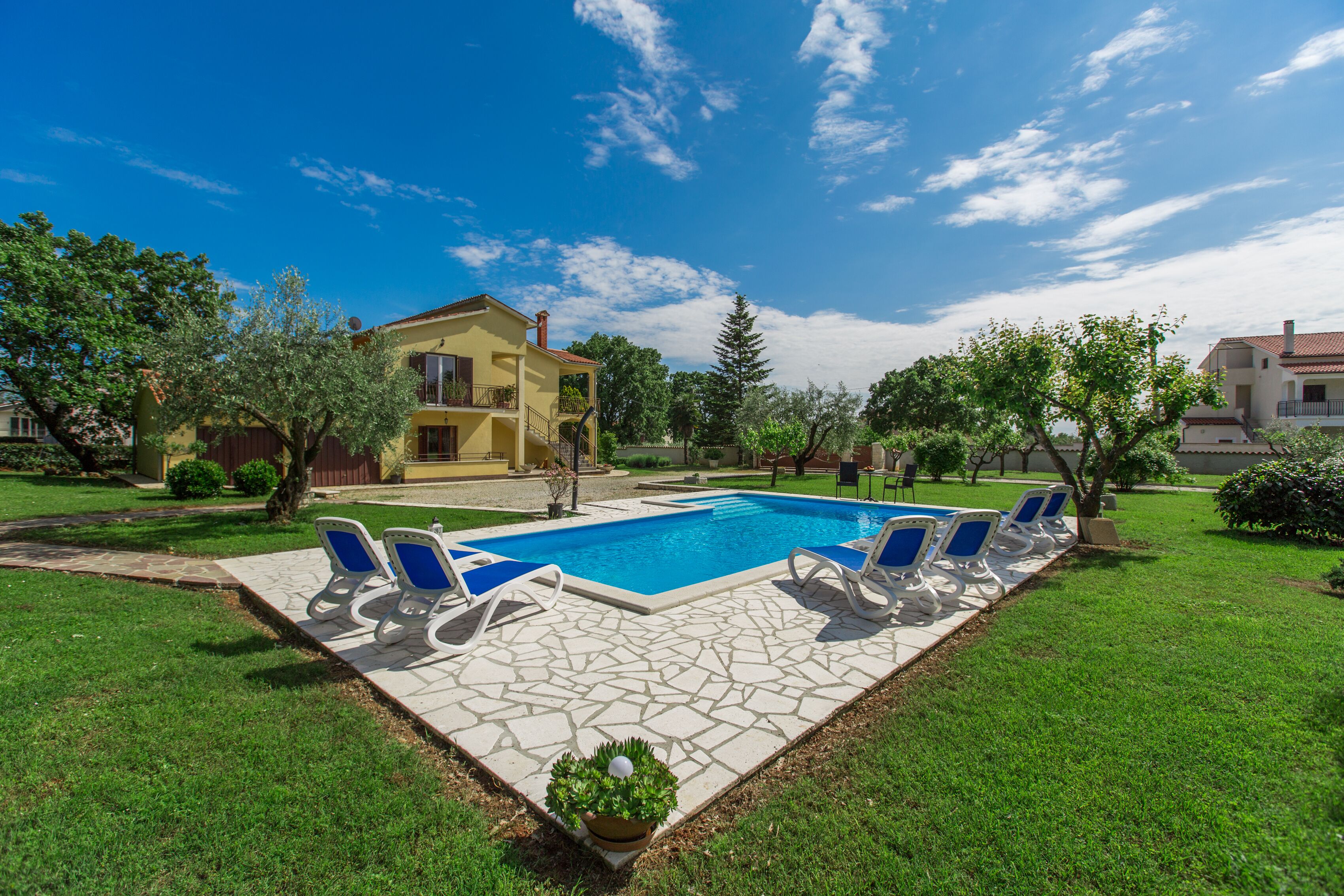 A swimming pool with lounge chairs, a stone deck, and a yellow building in the background.
