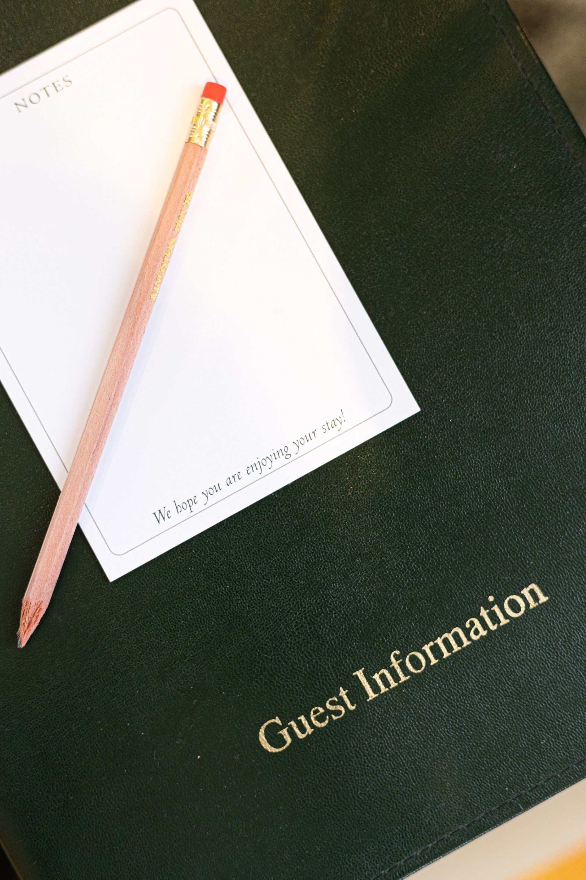 Um livro de informações para hóspedes preto, com um lápis e um cartão para anotações.