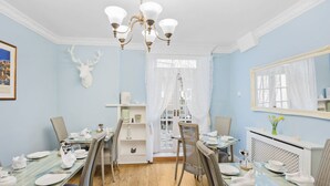A dining area with a wooden table set for six, surrounded by wicker chairs. A chandelier hangs from the ceiling, and a deer head decoration is mounted on the wall. - Kingston House (Torquay)