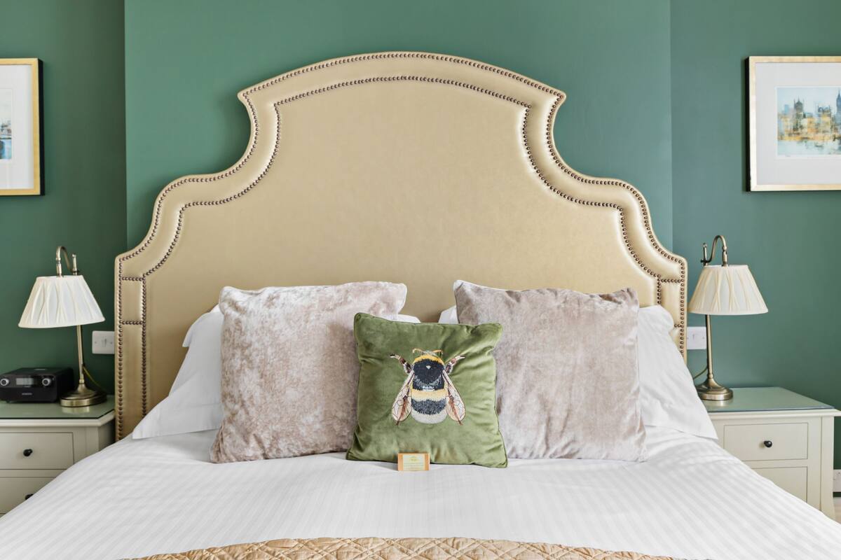 A neatly made bed with a beige headboard, two bedside lamps, and a green pillow with a bee design.