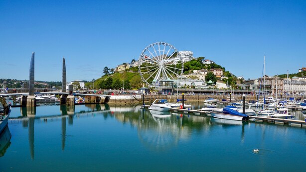 A marina with boats docked, a large Ferris wheel, and buildings in the background. - Kingston House (Torquay)