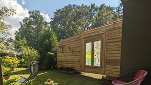 Eine Terrasse mit Holzdeck, zwei Korbstühle, einem Blumentopf und einem kleinen Garten.
