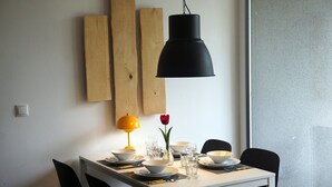 Ein Esstisch ist gedeckt mit Tellern, Schüsseln, Gläsern und Besteck. Eine gelbe Lampe, eine rote Tulpe und Holzpaneele sind an der Wand zu sehen.