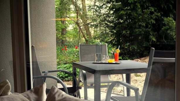 Eine Terrasse mit Tisch und Stühlen, einem Glas Orangensaft und einer Wasserflasche.