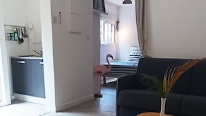 Un salon moderne avec un canapé foncé, une table basse en bois et une plante en pot. On aperçoit à l’arrière-plan un coin cuisine avec un évier et des placards.