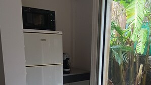 Une cuisine compacte équipée d’un four à micro-ondes et d’une machine à café, une porte coulissante donnant sur une terrasse en bois, et une vue sur une végétation luxuriante.