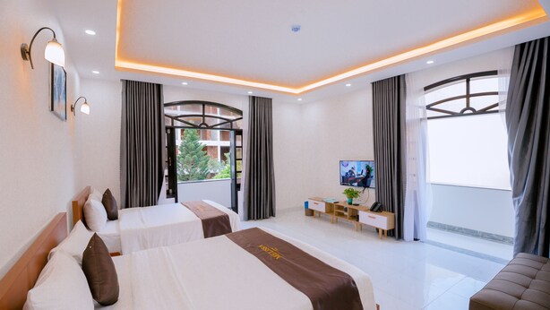 Une chambre d’hôtel moderne équipée de deux lits, d’un bureau, d’une télévision et de grandes fenêtres avec des rideaux.
