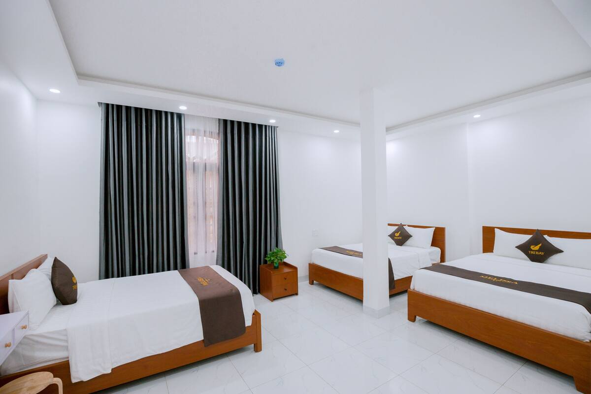 Una habitación de hotel con dos camas individuales, una mesita pequeña y un ventanal grande con cortinas.