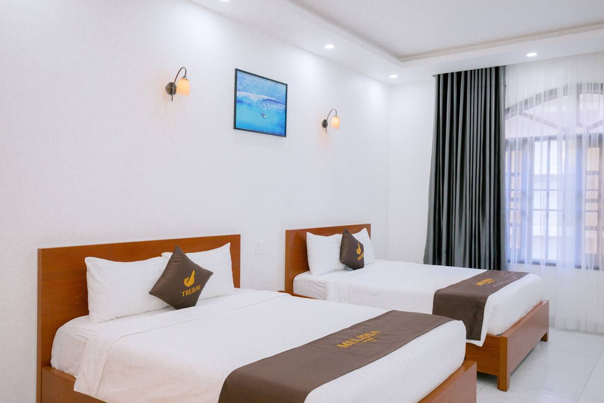 Habitación de hotel con dos camas, un cuadro enmarcado en la pared y una ventana con cortinas.