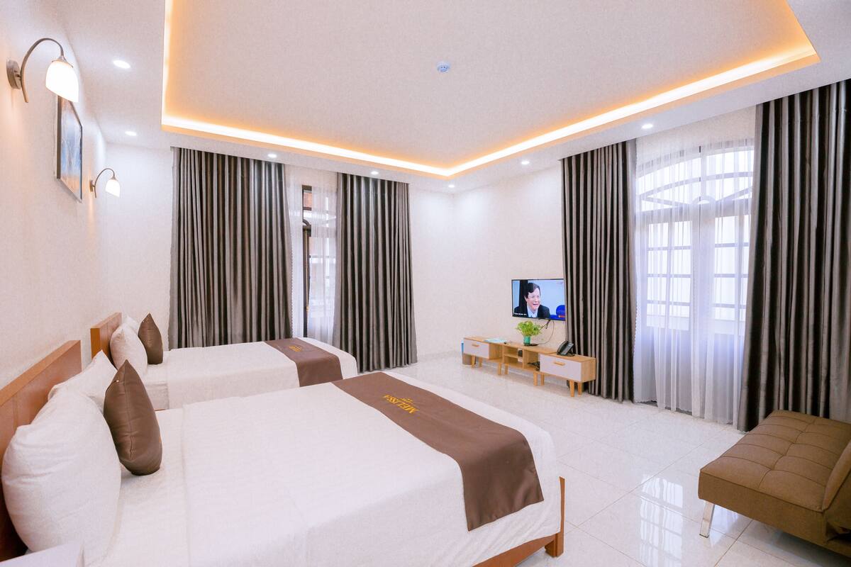 Habitación de hotel con dos camas, un escritorio, un televisor y cortinas.