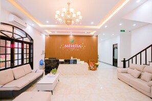 A hotel reception area with a reception desk, two sofas, a coffee table, a chandelier, and a wooden wall with the hotel name. - Melissa Hotel - Vung Tau (Ho Chi Minh City)