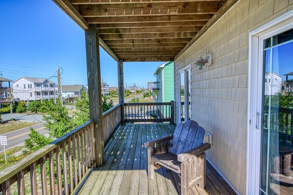 A wooden porch with a bench, a glass door, and a view of the neighborhood.