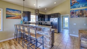 A modern kitchen with a central island, bar stools, and overhead pendant lighting. - Your Slice of Heaven on Topsail Island (Topsail Beach)