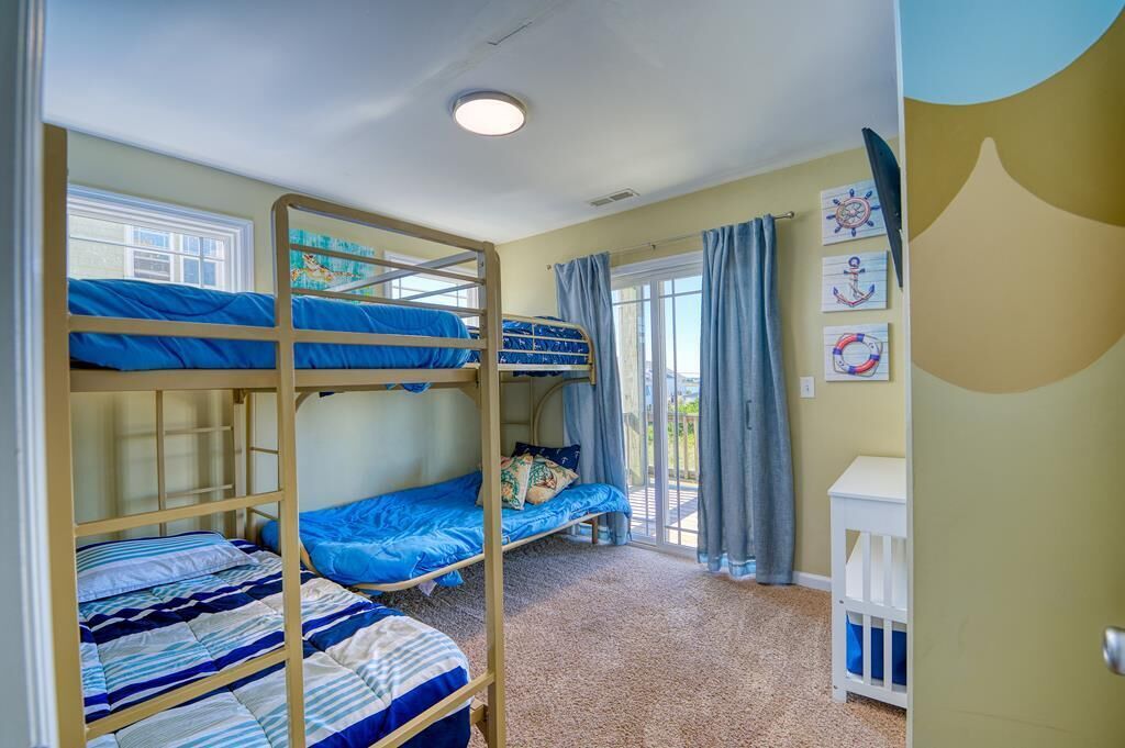 Une chambre avec un lit superposé, une fenêtre, des rideaux et des décorations murales sur le thème de la marine.