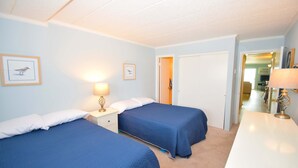 Une chambre d’hôtel avec deux lits, un bureau blanc et une porte donnant sur un couloir.