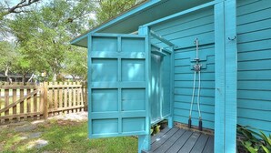 Un cobertizo azul con puerta de madera, un pequeño porche y una manguera conectada al costado.
