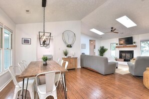 Amplia sala de estar con una mesa de comedor de madera, sillas blancas, un sofá gris y una chimenea.