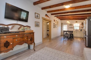 A spacious kitchen with wooden beams, a dining area with stools, and a large flat-screen TV mounted on the wall.