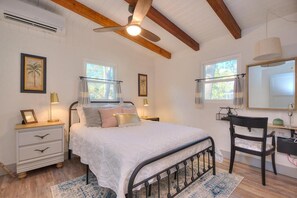 A bedroom with a bed, bedside tables, a desk, a chair, a ceiling fan, and two windows.