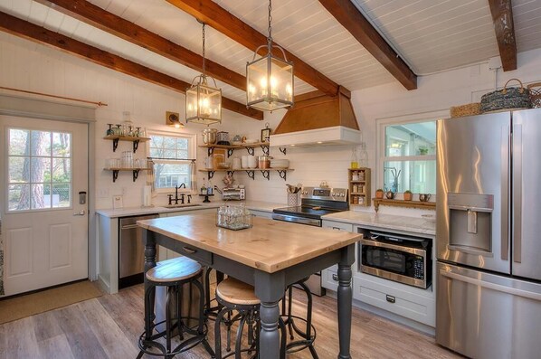 A kitchen with wooden beams, a central island with stools, stainless steel appliances, and hanging light fixtures.