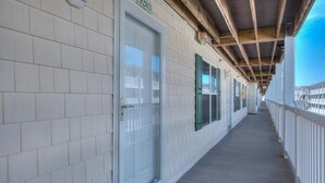A covered corridor with white tiled walls, a wooden floor, and a series of windows with green shutters. - Experience ocean views at the Oak Island OW 9203, a 2-bedroom condo for up to 6 guests. (Oak Island)