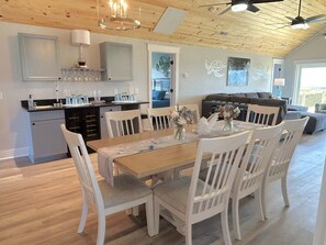 A dining area with a wooden table and white chairs, a kitchen with grey cabinets, and a living area with a sofa and a ceiling fan.