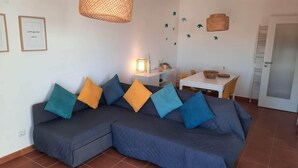 A modern living room with a sectional sofa, a small dining table, and a wall-mounted lamp. - Beach House MONTE CLÉRIGO (Aljezur)