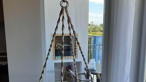 A room with a hanging chair, a window with a view, and a tiled floor. - Beach House MONTE CLÉRIGO (Aljezur)