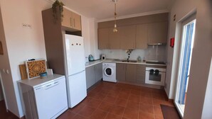 A compact kitchen with a washing machine, a built-in oven, and a sink. - Beach House MONTE CLÉRIGO (Aljezur)