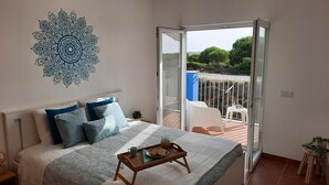 A bedroom with a bed, a bedside table, a tray with breakfast items, and a view of the outdoors through a sliding glass door. - Beach House MONTE CLÉRIGO (Aljezur)
