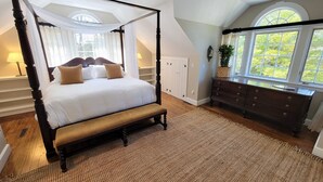 Una cama con dosel y cuatro columnas, acompañada de un banco, un aparador y una ventana que ofrece vistas a zonas verdes.