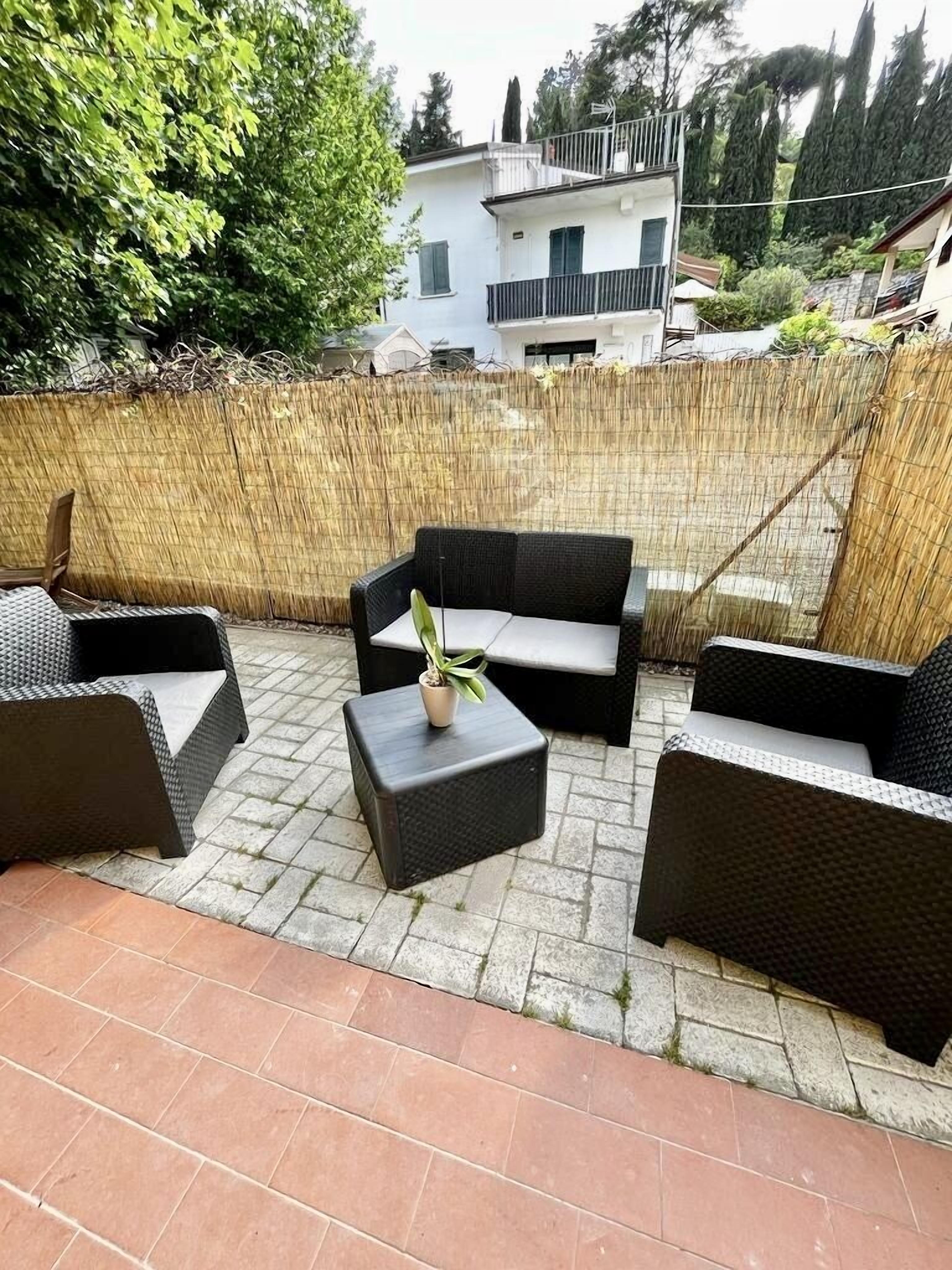 Ein möblierter Patio im Freien mit Korbmöbeln, darunter eine Sitzecke und zwei Sessel, sowie ein kleiner Tisch mit einer Pflanze.