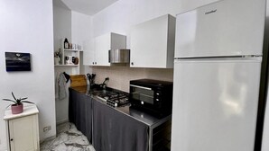 Una cucina compatta con mobili bianchi, forno a incasso, microonde e frigorifero.
