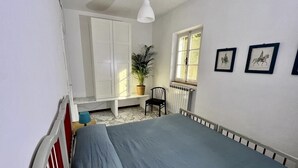 Una camera da letto con un letto, una finestra, un termosifone, una sedia e una pianta in vaso.