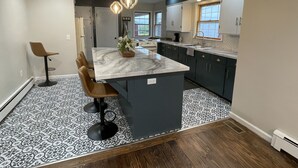 A modern kitchen with a marble island, dark cabinetry, and patterned flooring. - Highland Hills- Family, Farm, Golf and Goats (Ubly)