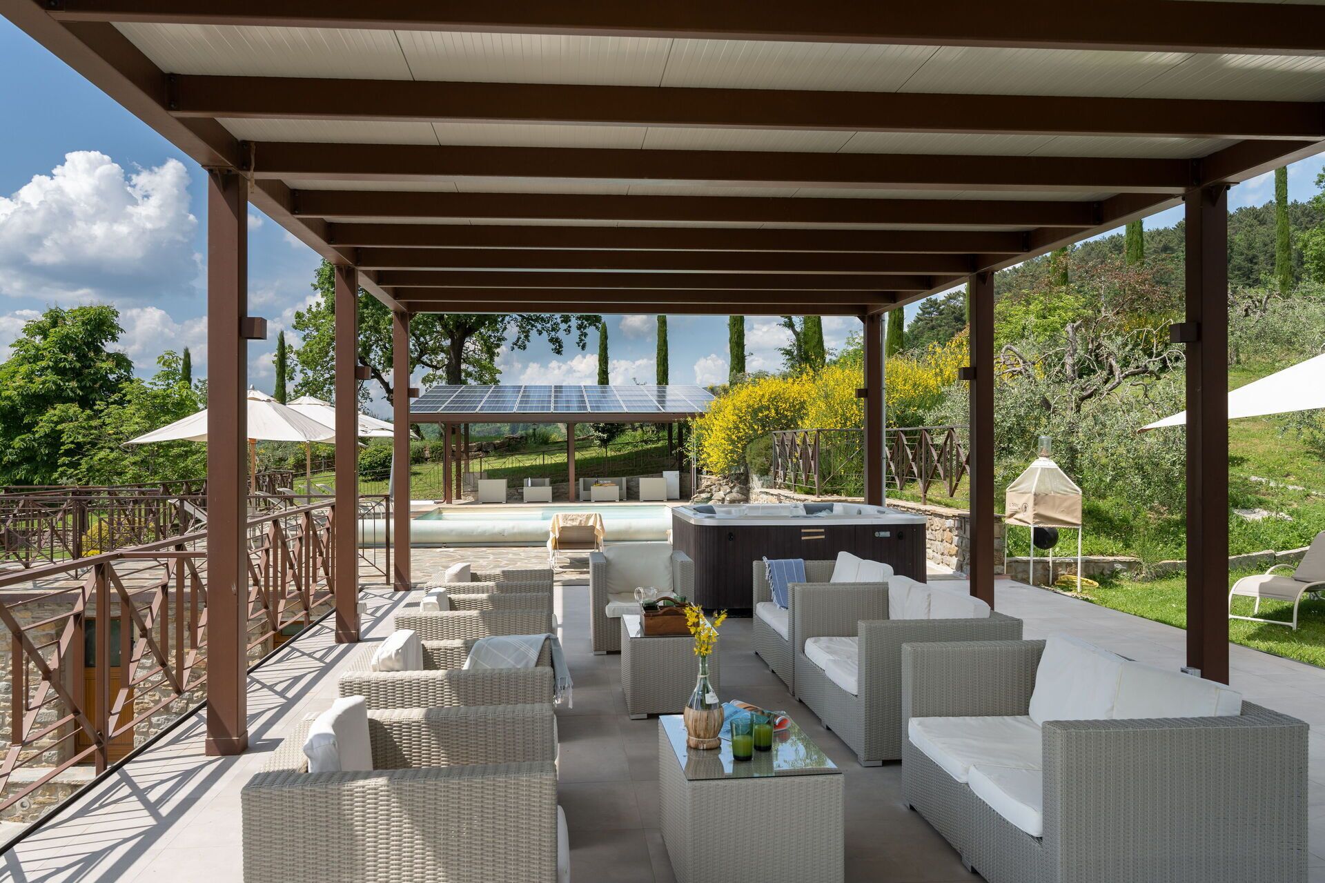 A covered outdoor seating area with wicker furniture, a hot tub, and solar panels.