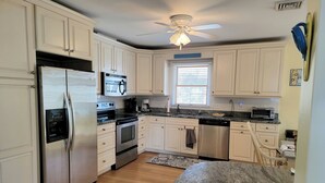 A modern kitchen with white cabinets, stainless steel appliances, a granite countertop, and a ceiling fan. - 6 Bedroom ocean block home with private beach access (Bethany Beach)