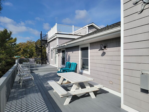 A deck with outdoor seating, a staircase, and a building with a grey siding exterior.