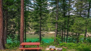 A picnic table in a forested area with a view of a green lake. - Welcome to Sweet Water, 2 bed 2 bath log cabin 10 minutes from Glacier Park! (Hungry Horse)