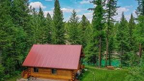 A wooden cabin with a red roof surrounded by dense forest. - Welcome to Sweet Water, 2 bed 2 bath log cabin 10 minutes from Glacier Park! (Hungry Horse)