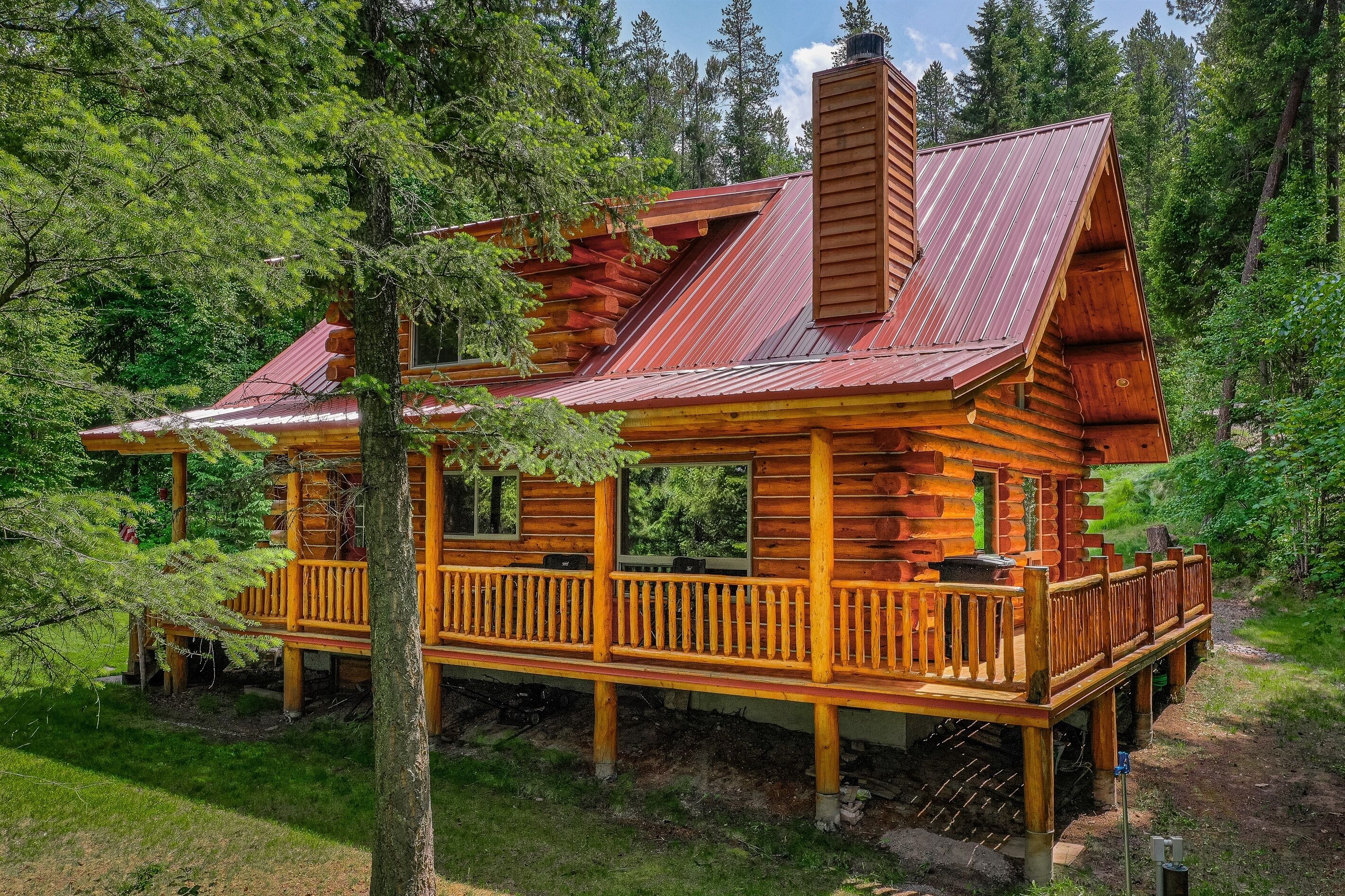 Une cabane en rondins avec une terrasse en bois, une cheminée et un porche.
