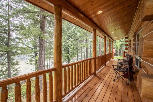 A wooden deck with a railing, overlooking a forested area and a body of water.