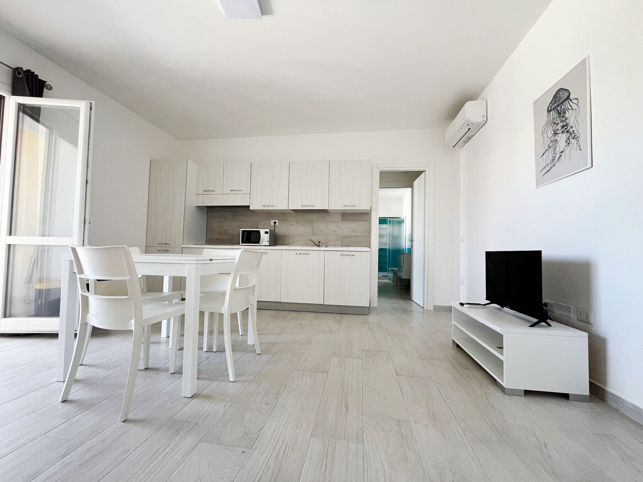 A modern kitchen with white cabinets, a microwave, and a dining area with white chairs.