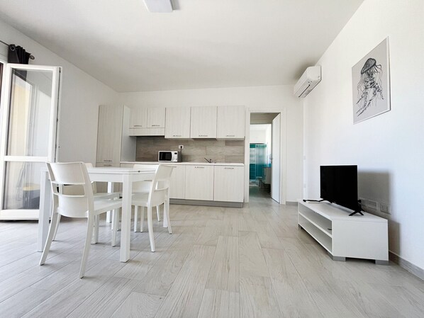 A modern kitchen with white cabinets, a microwave, and a dining area with white chairs.