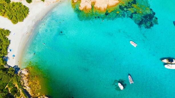 Vista aerea di una zona costiera con acque cristalline turchesi, spiagge sabbiose e imbarcazioni ancorate vicino alla riva.