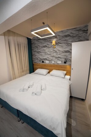 Una habitación de hotel con una cama bien hecha, un cabecero con una pared de aspecto marmolizado, un armario y una lámpara en el techo.