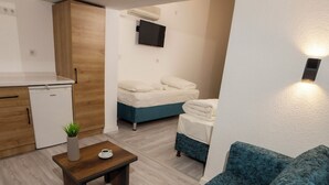Espaço compacto com cozinha americana, sofá, uma pequena mesa com uma planta e uma cama com cabeceira azul.