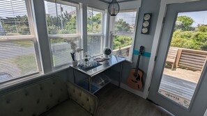 A cozy room with a large window, a guitar, and a small table with decorative items. - Stylish beach box freshly renovated and redesigned (Rodanthe)