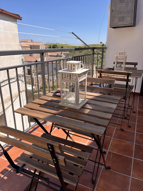 A terrace with wooden benches and a table, a lantern, and a view of wind turbines in the background.